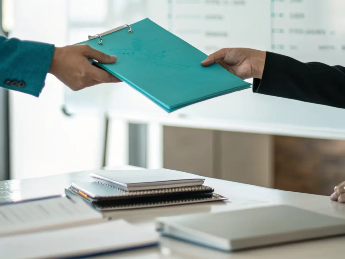 Remise d’un dossier structuré entre deux personnes lors d’une passation, organigramme au tableau